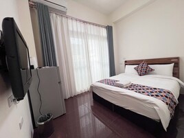 Een hotelkamer met een bed, een televisie, een koelkast en een raam met gordijnen.