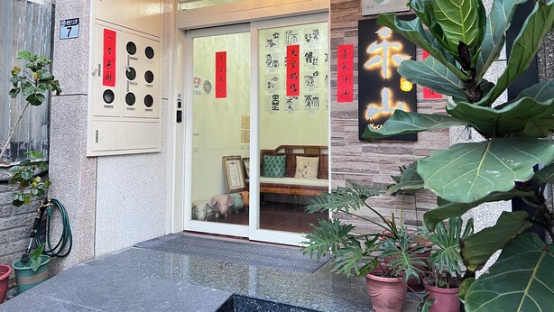A building entrance with a door, a wall-mounted elevator, and several potted plants. - HeShan B&B (Hualien City)