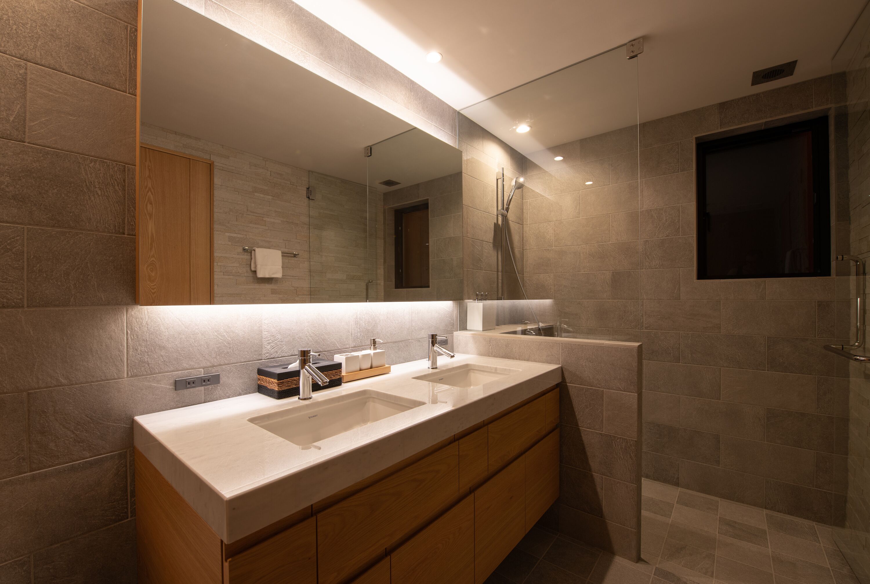 Une salle de bain moderne avec un meuble-lavabo à deux vasques, des armoires en bois, un grand miroir et un espace douche.