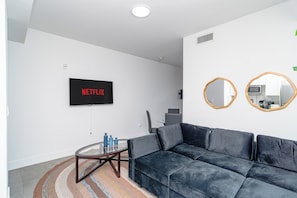 Una sala de estar moderna con un sofá azul oscuro, una mesa de centro de vidrio y un televisor de pantalla plana montado en la pared que muestra