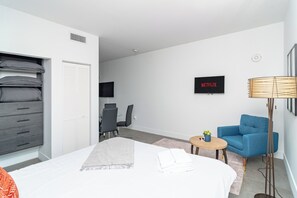 Una habitación de hotel moderna con cama, escritorio, silla, televisor y lámpara.
