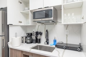 Una cocina moderna con microondas integrado, pileta de acero inoxidable y diversos utensilios de cocina.