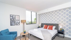 Ein modernes Schlafzimmer mit einem großen Bett, einem blauen Sessel, einem runden Beistelltisch und einer Wand mit Muster-Tapete.