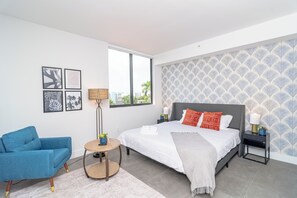 Ein modernes Schlafzimmer mit einem großen Bett, einem blauen Sessel, einem runden Beistelltisch und einer Wand mit Muster-Tapete.