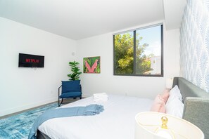 Ein Hotelzimmer mit Bett, Sessel, Fernseher und einem Fenster mit Blick auf Bäume.