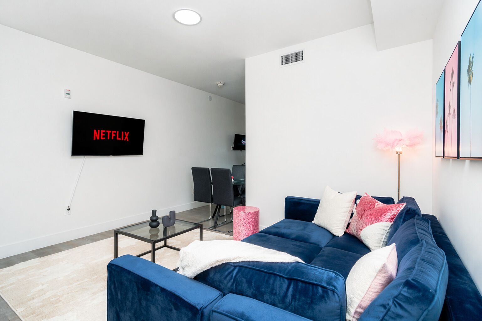 A living room with a blue sofa, a glass coffee table, a flat-screen TV, and a pink lamp.