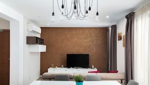 Een moderne woonkamer met een witte bank, een flatscreen televisie, een eettafel met stoelen en een plafondlamp.