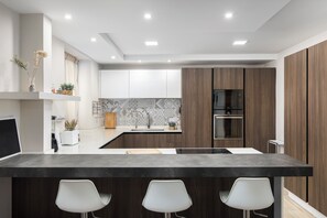A modern kitchen with a central island, white bar stools, a microwave, and an oven. - Luxury Msida Circle Suites (Mgarr)