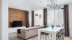 Een moderne woonkamer met een bank, een eettafel met stoelen, een televisie en een kroonluchter.