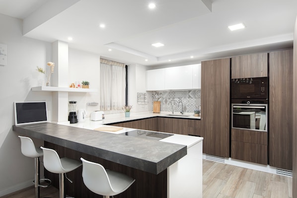 Una cocina moderna con una isla central, taburetes de bar, horno integrado y microondas.