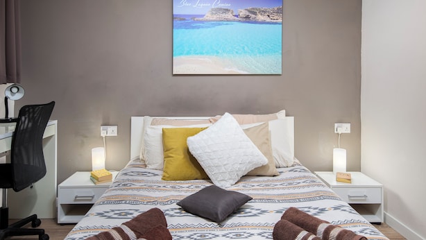 Een slaapkamer met een bed, nachtkastjes, een bureau en een stoel.