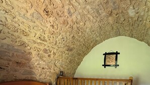 Ein Schlafzimmer mit Steinwand, einem hölzernen Bett, einem kleinen Holzstuhl und einem Nachttisch mit Lampe.