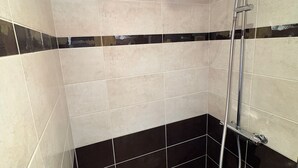 Ein Badezimmer mit beige- und schwarzen Fliesen, einer Dusche mit Duschbrause und einer kleinen Shampooflasche auf dem Boden.