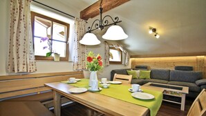 Un comedor con una mesa de madera dispuesta para dos personas, un sofá y una ventana con cortinas.