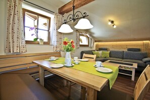 A dining area with a wooden table set for two, a sofa, and a window with curtains. - Vacation apartment Morg'n-Liacht, 75 sqm, 2 bedrooms, balcony and WLAN (Siegsdorf)