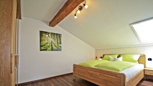 Un dormitorio con una cama de madera, una mesita de noche, una lámpara de pared y un ventanal grande.
