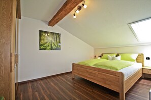 A bedroom with a wooden bed, a nightstand, a wall-mounted light fixture, and a large window. - Vacation apartment Morg'n-Liacht, 75 sqm, 2 bedrooms, balcony and WLAN (Siegsdorf)