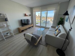 A modern living room with a flat-screen TV, a sofa, a coffee table, and a floor lamp. - Swing &Sun Free Parking by StayCare (Chipiona)