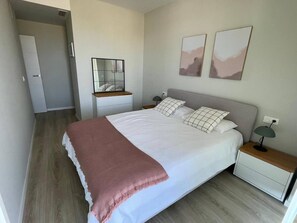 Ein Schlafzimmer mit einem großen Bett, Nachttischen, einem Spiegel und zwei an der Wand befestigten Kunstwerken.