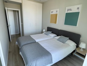 Quarto de hotel com uma cama, duas mesas de cabeceira, um guarda-roupa e duas amostras de cores fixadas na parede.