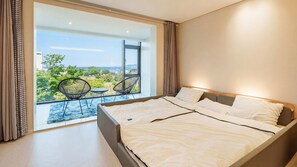 Une chambre avec un grand lit, un balcon avec des chaises et une vue sur la verdure.