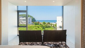 Une chambre avec une grande fenêtre, un lit et une vue sur la mer et les bâtiments.
