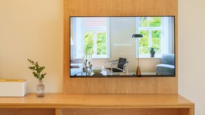 A modern room with a large TV mounted on a wooden wall, a desk with a vase, and a window with a view of greenery.