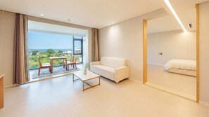 A modern hotel room with a white sofa, a small table, and a view of the sea.