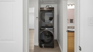 Ein Waschraum mit gestapelten Waschmaschinen und Trocknern, einem Waschbecken und einer Tür zu einem Badezimmer.
