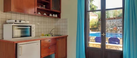 Una cocina con armarios de madera, microondas, refrigerador y ventana con cortinas.