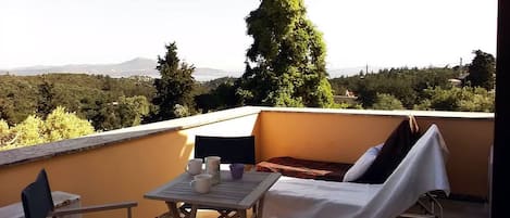 A balcony with a table, chairs, and a covered lounge chair.