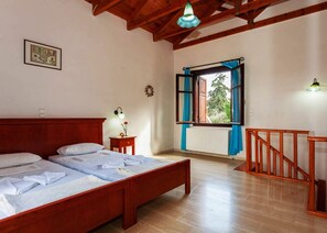 A bedroom with a wooden bed, a nightstand, a window with blue curtains, and a wooden staircase.