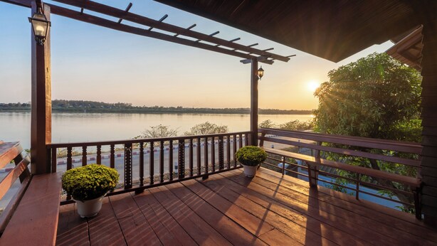 A wooden deck with a pergola, potted plants, and a view of a calm lake at sunset.