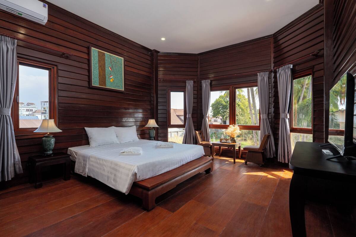 A wooden-paneled bedroom with a large bed, bedside tables, a desk, and a view of the outdoors.