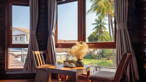 A room with a wooden table, chairs, a vase with dried flowers, and large windows with curtains.