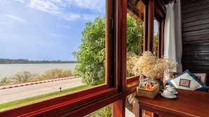 A wooden balcony with a view of a lake, a wicker basket with bottles, and a decorative pillow.