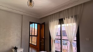 Un dormitori amb un llit, una petita taula de nit, una làmpada penjant, una finestra amb cortines i vista a l'exterior.