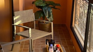 Un balcó amb una cadira, una planta en test i un safata amb una ampolla d'aigua, una tassa i una tetera.