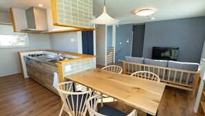 A modern kitchen with a wooden table and chairs, a built-in stove, and a dining area with a sofa and TV. - Furano Entire House｜Ski & Lavender｜Mountain View｜Groups up to 10 ｜ 3BR (Furano City)