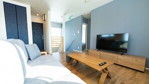 A modern living room with a sofa, a wooden coffee table, a TV, and a staircase leading to another room. - Furano Entire House｜Ski & Lavender｜Mountain View｜Groups up to 10 ｜ 3BR (Furano City)