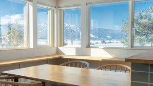 A room with a wooden table and chairs, large windows with a view of snow-covered mountains. - Furano Entire House｜Ski & Lavender｜Mountain View｜Groups up to 10 ｜ 3BR (Furano City)
