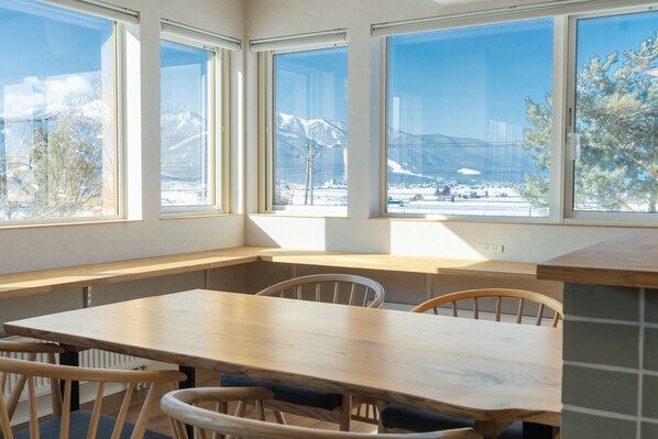 A room with a wooden table and chairs, large windows with a view of snow-covered mountains.