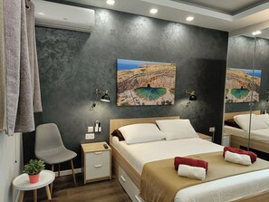 A bedroom with a bed, bedside tables, a chair, a small table with a plant, and a wall-mounted air conditioner. - Cosy Albert's Seaside Suites - Sliema (Gżira)