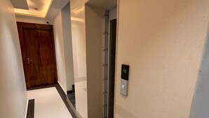 A modern hallway with a wooden door, an elevator, and a wall-mounted control panel.