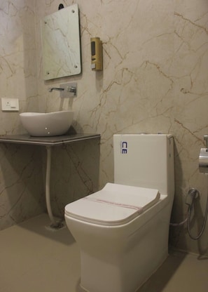 A bathroom with a white toilet, a white sink, a marble wall, and a mirror. - Hotel Gorli Heritage (Roorkee)