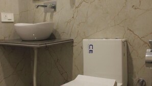 A bathroom with a white toilet, a white sink, a marble wall, and a mirror.