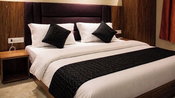 A neatly made bed with a dark headboard, white bedding, and a black quilted throw.