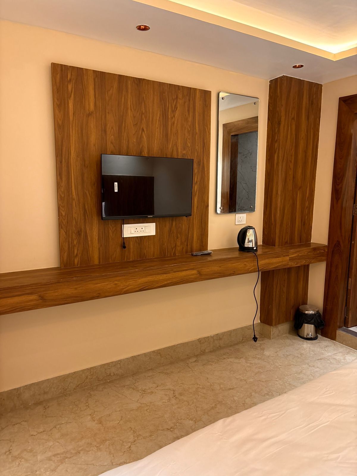 Habitación de hotel con tocador de madera, televisor de pantalla plana, espejo, cafetera y un cubo de basura.