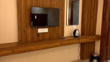 Habitación de hotel con tocador de madera, televisor de pantalla plana, espejo, cafetera y un cubo de basura.