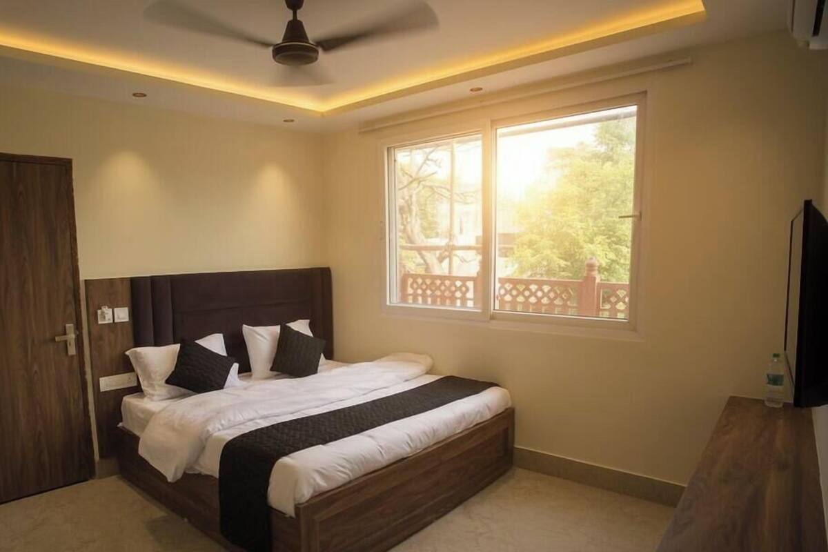 A bedroom with a bed, a ceiling fan, a window with a view, and a wooden door.